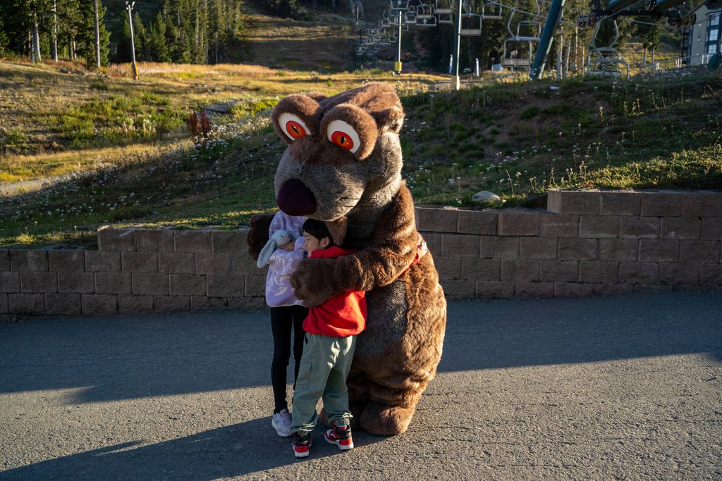 Two children having a hug with the Monster Marmot Mascot.