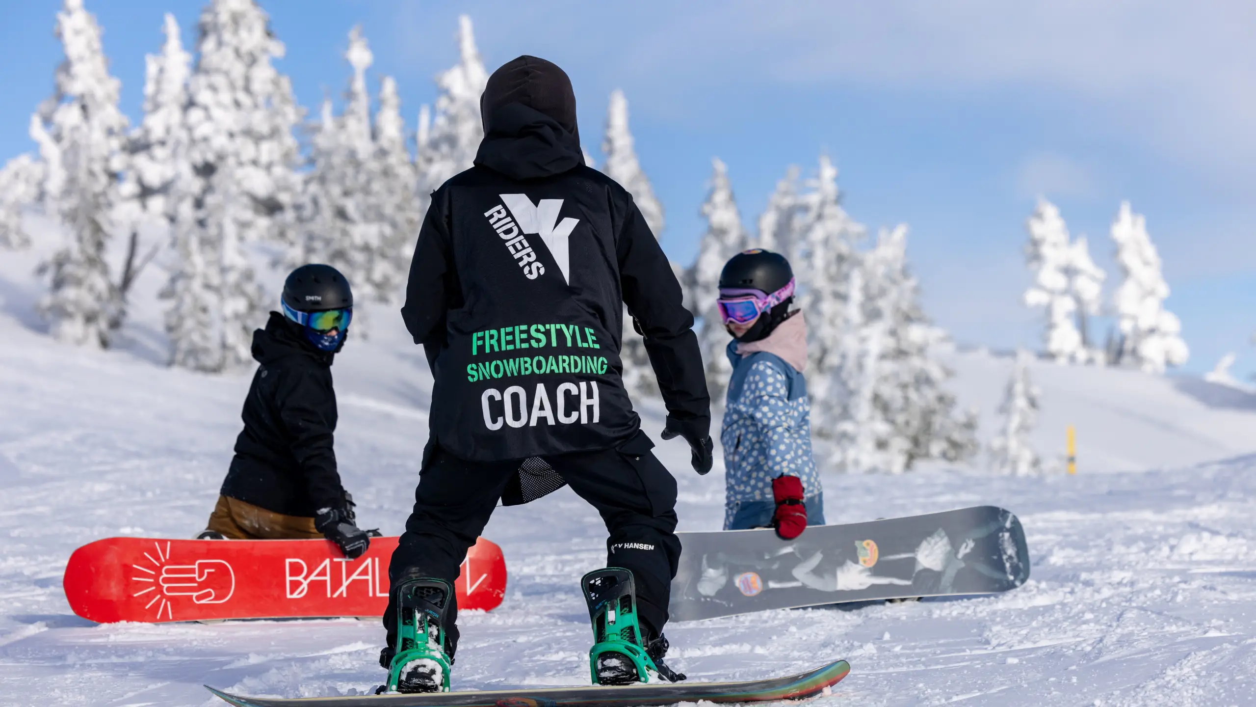 Young snowboarders receiving instructions from a VI Riders snowboard coach